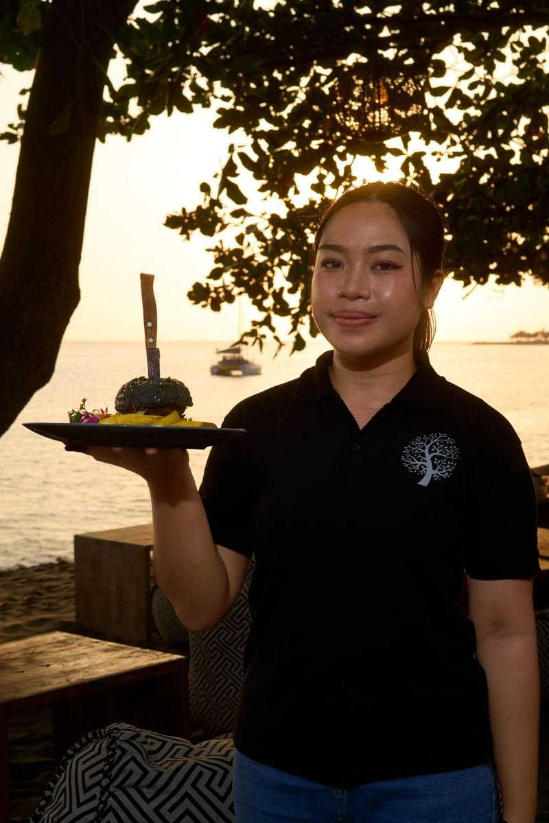A JOJE team member with a black-bun burger at sunset